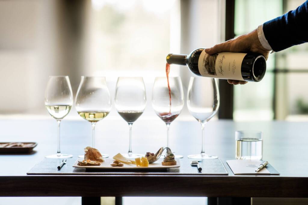 Pouring Knights Bridge white and red wines into glasses on sun-lit table with plate of elegant nibbles.