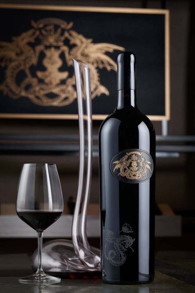Single large-format Draco Dormiere bottle with gold printing on glass, next to tall decanter.