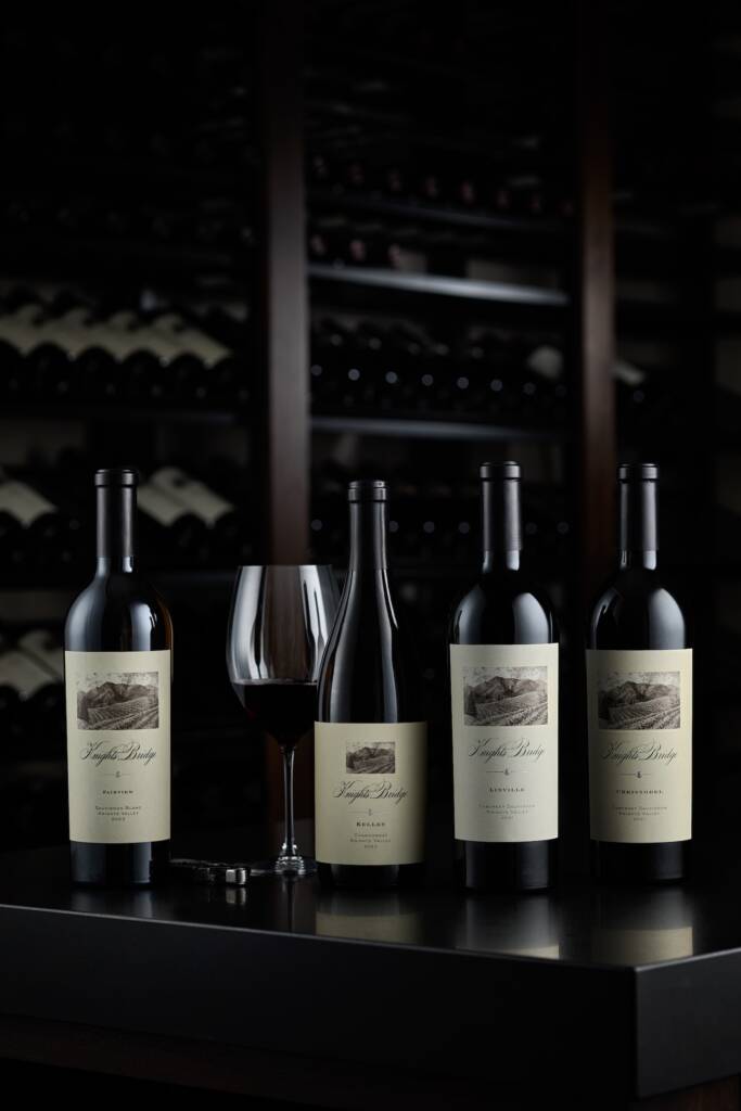 Vineyard Collection wines with glass in dark wine cellar.