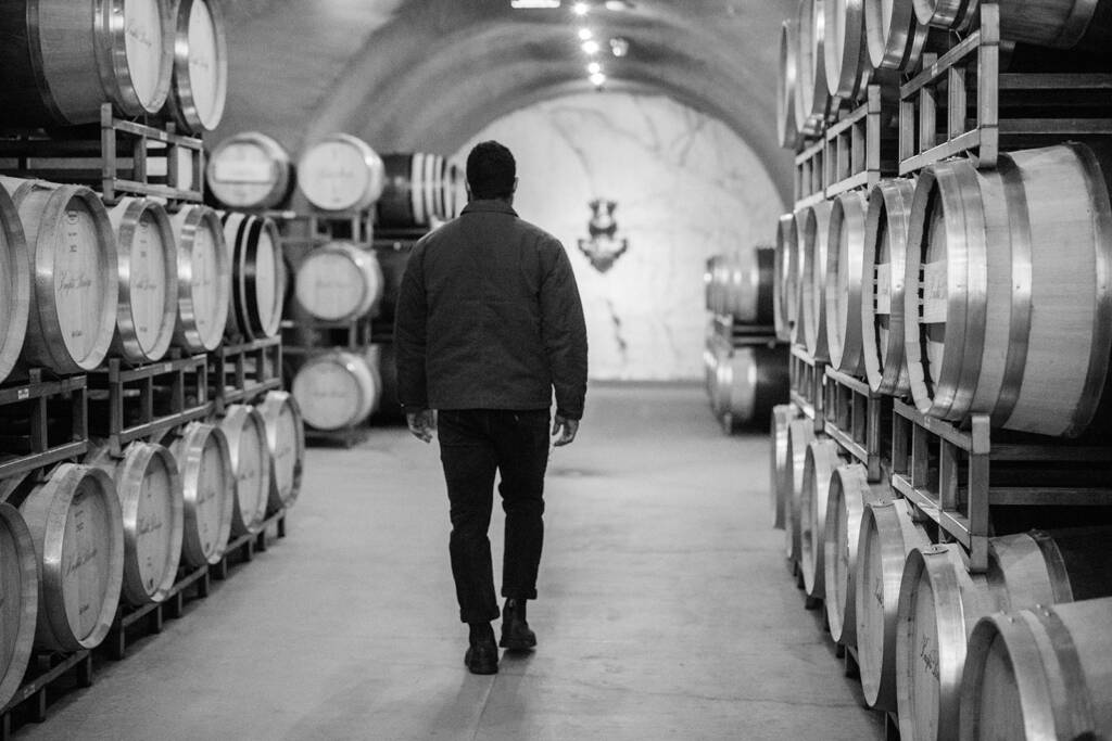 Black and white image of Derek's back as he walks past barrels in the winery